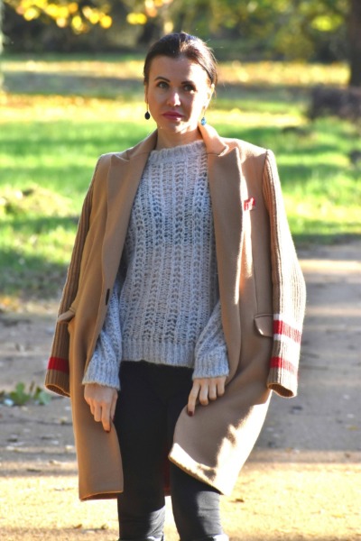 Mujer con parca en color marrón claro, jersey gris y detalles rojos durante la temporada otoño invierno